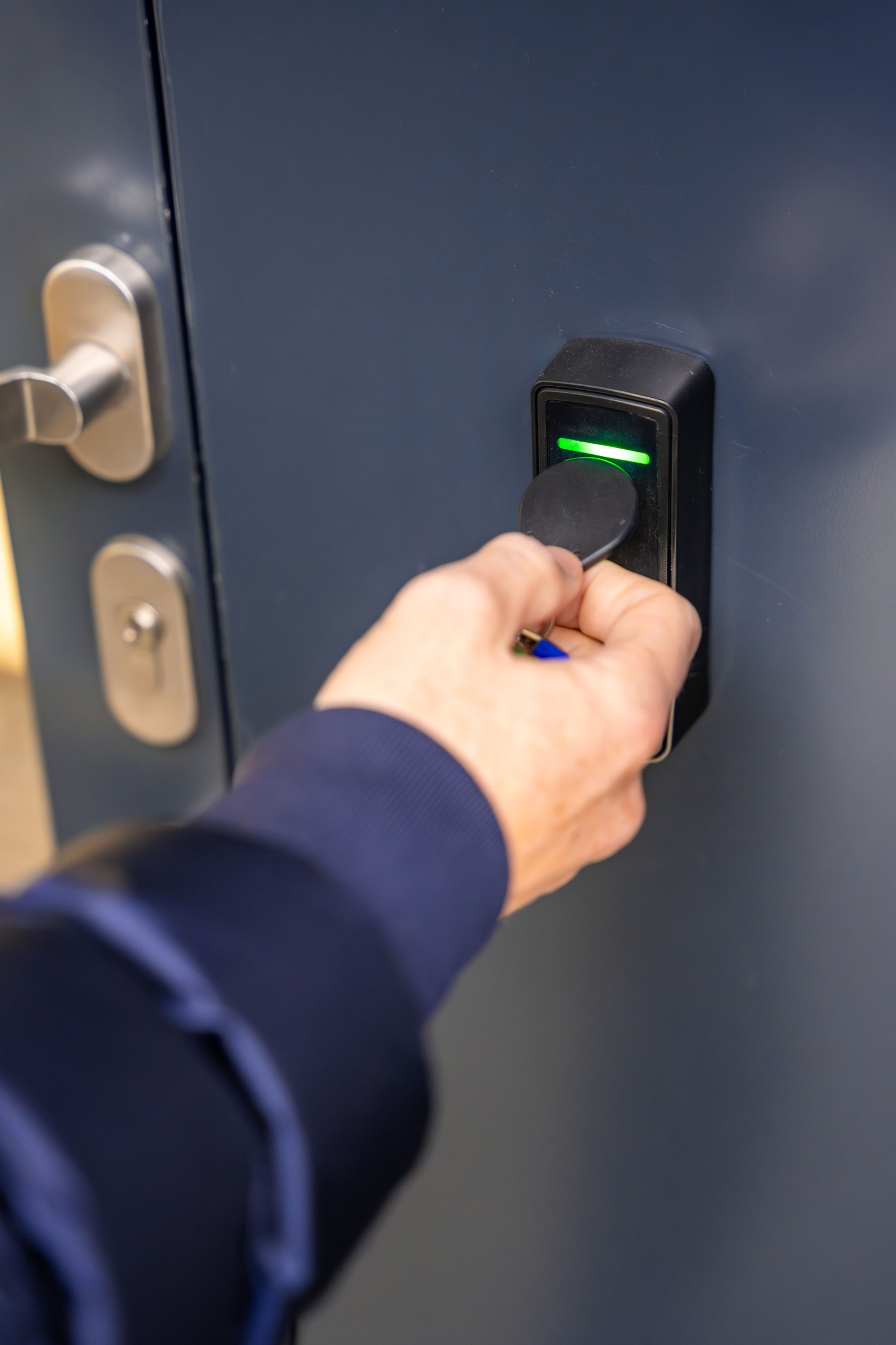 Close up view of person using a electric lock key fob to access a building via a reader of entry system mounted on a house wall